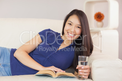 Beautiful asian girl lying on the sofa reading a novel and drink