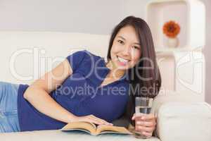 Beautiful asian girl lying on the sofa reading a novel and drink