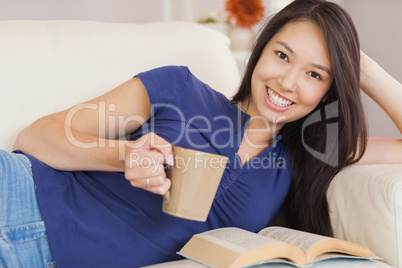 Attractive young asian woman lying on the sofa reading a novel a