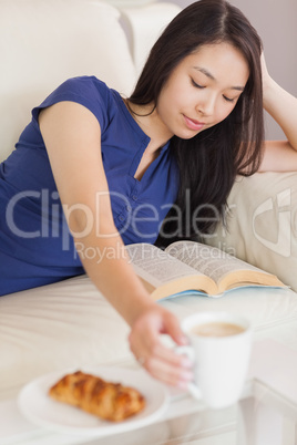 Pretty young asian woman lying on the sofa reading a book reachi