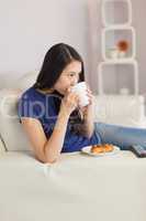 Woman sitting on the sofa drinking coffee with a pastry
