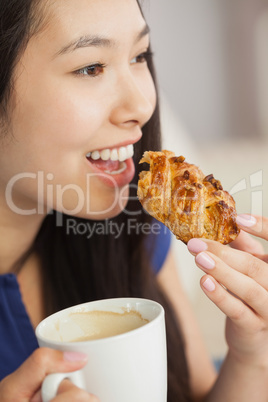 Young asian woman eating a pastry with a cup of coffee