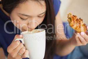 Young asian woman sipping her coffee and holding a pastry