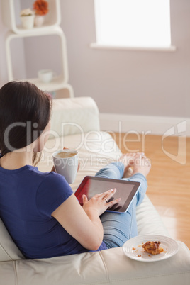 Young woman using her tablet pc and holding cup of coffee