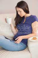 Young woman using her tablet pc and holding mug of coffee