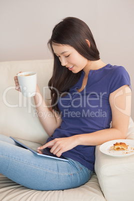 Young asian woman using her tablet pc and holding mug of coffee