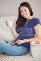 Young happy asian woman using her tablet pc and holding mug of c