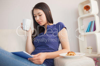 Young pretty asian woman using her tablet pc and holding mug of