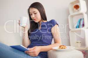 Young pretty asian woman using her tablet pc and holding mug of