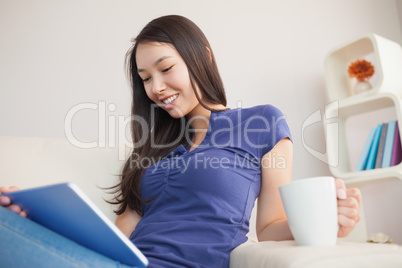 Young attractive asian woman using her tablet pc and holding mug