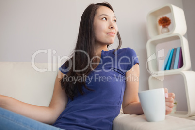 Attractive young asian woman sitting on the couch holding mug