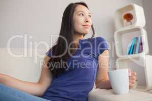 Attractive young asian woman sitting on the couch holding mug