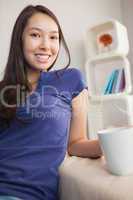 Happy young asian woman sitting on the couch holding mug