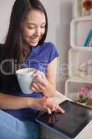 Happy asian woman sitting on the couch holding mug of coffee usi