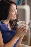 Happy asian woman sitting on the couch holding mug of coffee loo