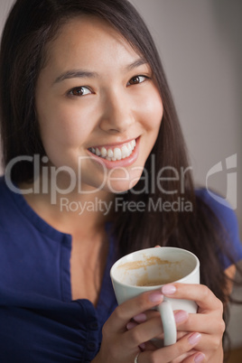 Happy asian woman holding mug of coffee looking at camera