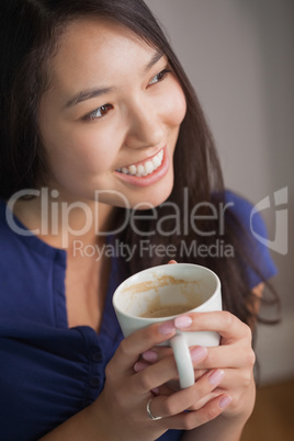 Smiling asian woman holding mug of coffee looking away