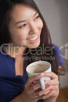 Smiling asian woman holding mug of coffee looking away