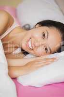 Pretty young asian woman lying in her bed smiling at the camera