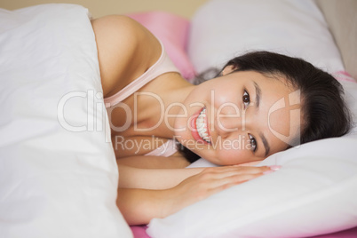 Happy young asian woman lying in her bed smiling at the camera