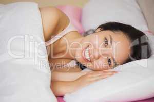 Happy young asian woman lying in her bed smiling at the camera