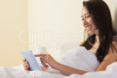 Smiling young asian woman sitting in bed using tablet pc