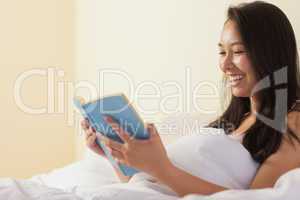 Smiling young asian woman sitting in bed reading a book