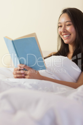 Pretty young asian woman sitting in bed reading a book