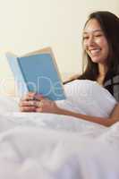 Pretty young asian woman sitting in bed reading a book