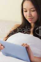 Pretty young asian woman sitting in bed using her digital tablet