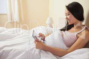 Smiling young asian woman sitting in bed using her digital table