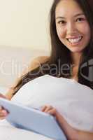 Pretty young asian woman sitting in bed using her digital tablet