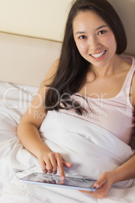 Cheerful young asian woman sitting in bed using her digital tabl