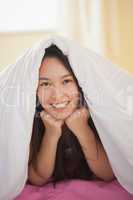 Cute young asian woman under her duvet smiling at camera