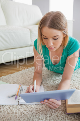 Attractive woman lying on floor using tablet to do her assignmen