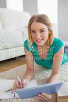 Happy woman lying on floor using tablet to do her assignment