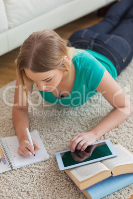 Focused young woman lying on floor using tablet to do her assign