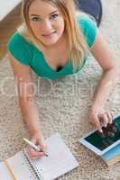 Happy woman lying on floor doing her homework using tablet