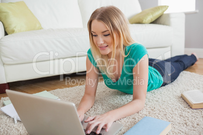 Happy woman lying on floor doing her homework using laptop