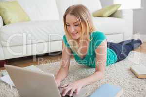 Happy woman lying on floor doing her homework using laptop