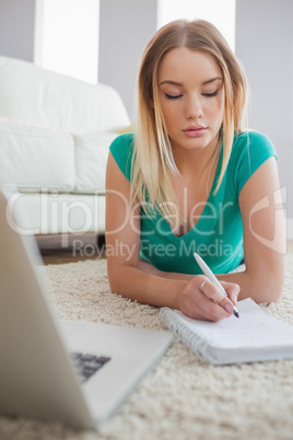 Concentrating woman lying on floor doing her homework using lapt