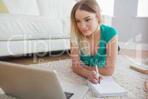 Smiling blonde lying on floor doing her homework using laptop