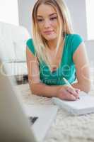 Smiling woman lying on floor doing her homework using laptop