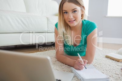 Happy blonde lying on floor doing her assigment using laptop