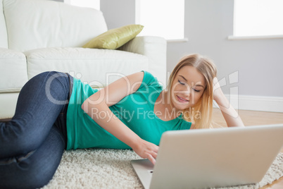 Smiling woman lying on floor using laptop