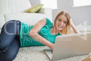 Happy woman lying on floor looking at laptop screen