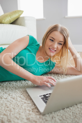 Attractive blonde woman lying on floor using laptop