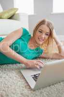 Attractive blonde woman lying on floor using laptop