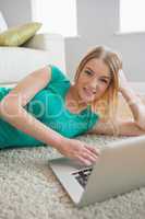 Smiling woman lying on floor using laptop