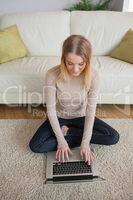 Blonde woman sitting on floor using laptop